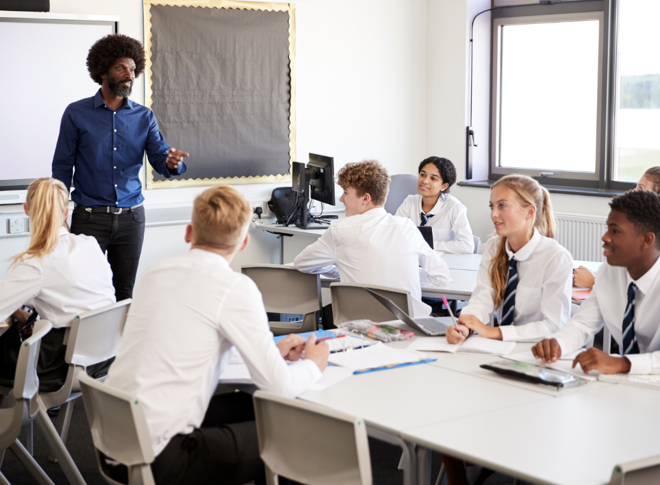 Image of teacher pointing whilst teaching to a classroom with students.